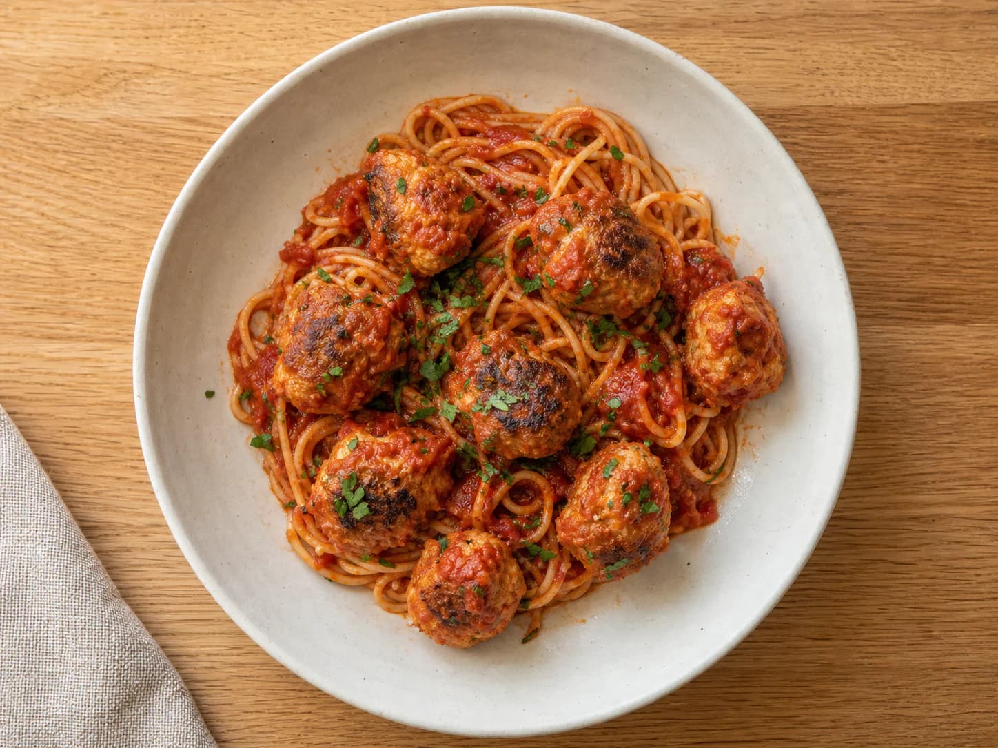 Spaghetti and marinara topped with browned baked chicken meatballs and parsley.