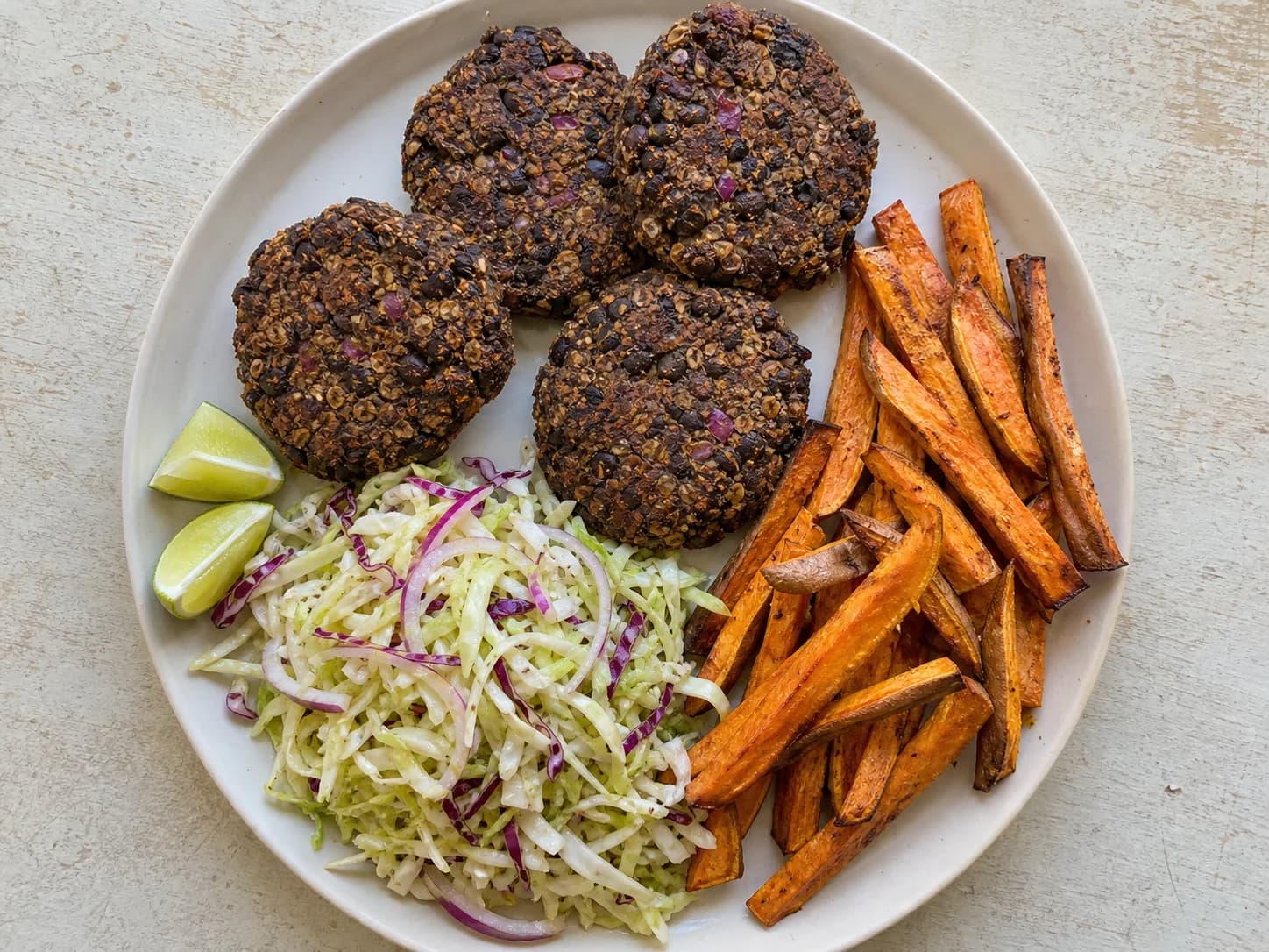 Overhead view of black-bean burger patties & oven fries, served as a family dinner.