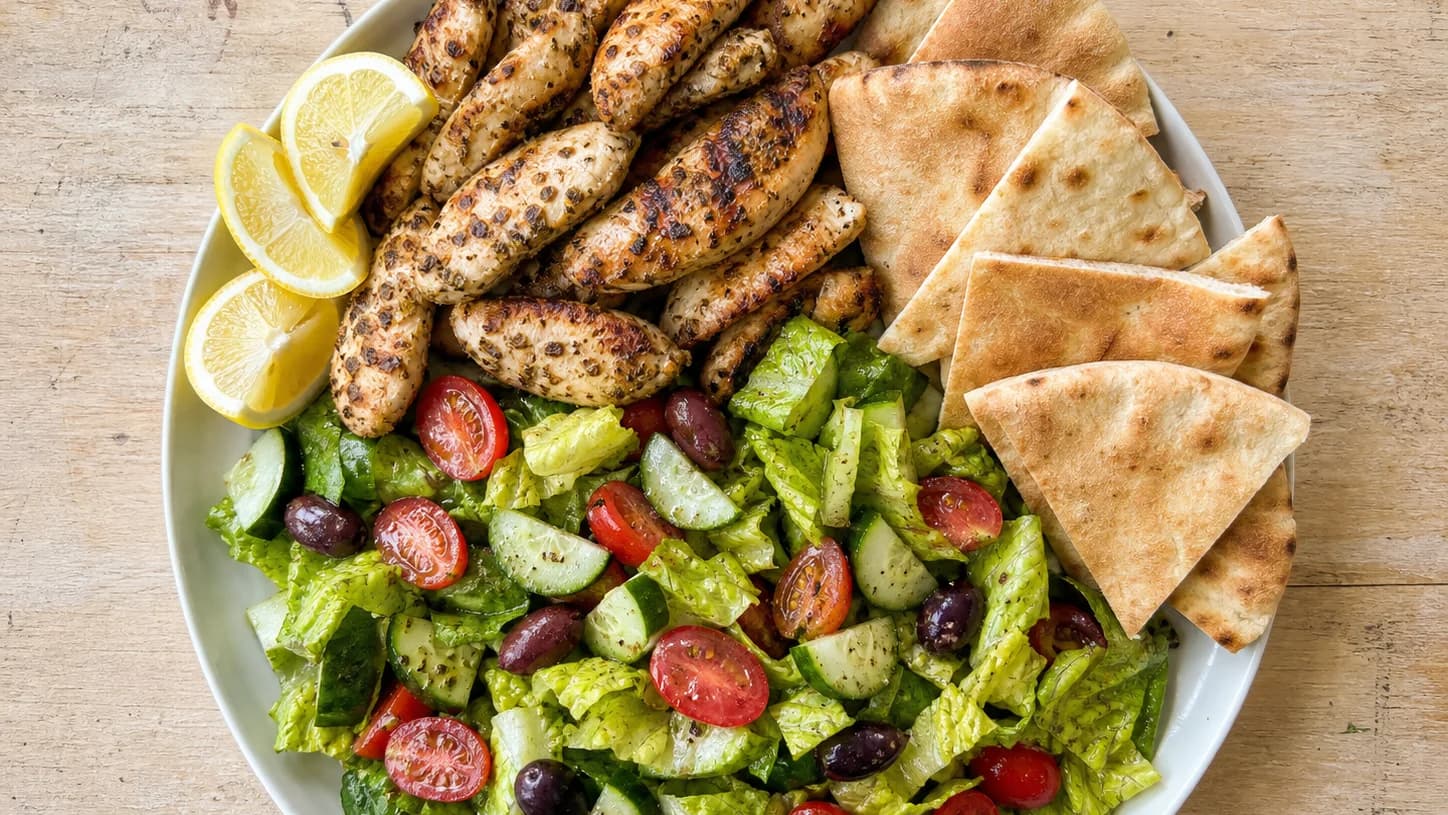Overhead view of greek lemon chicken pita plates, served as a family dinner.