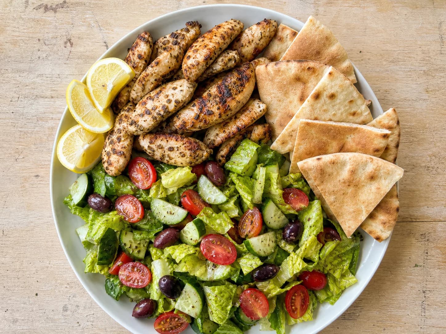Overhead view of greek lemon chicken pita plates, served as a family dinner.
