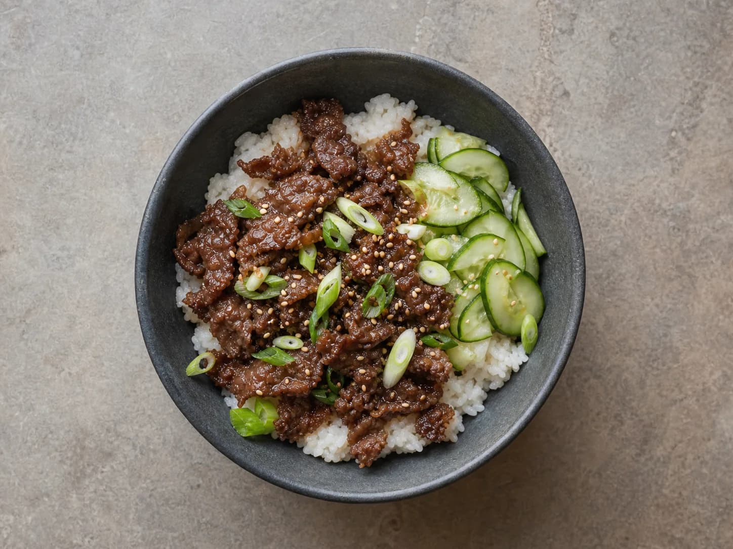 Overhead view of korean-inspired beef & cucumber rice bowls, served as a family dinner.