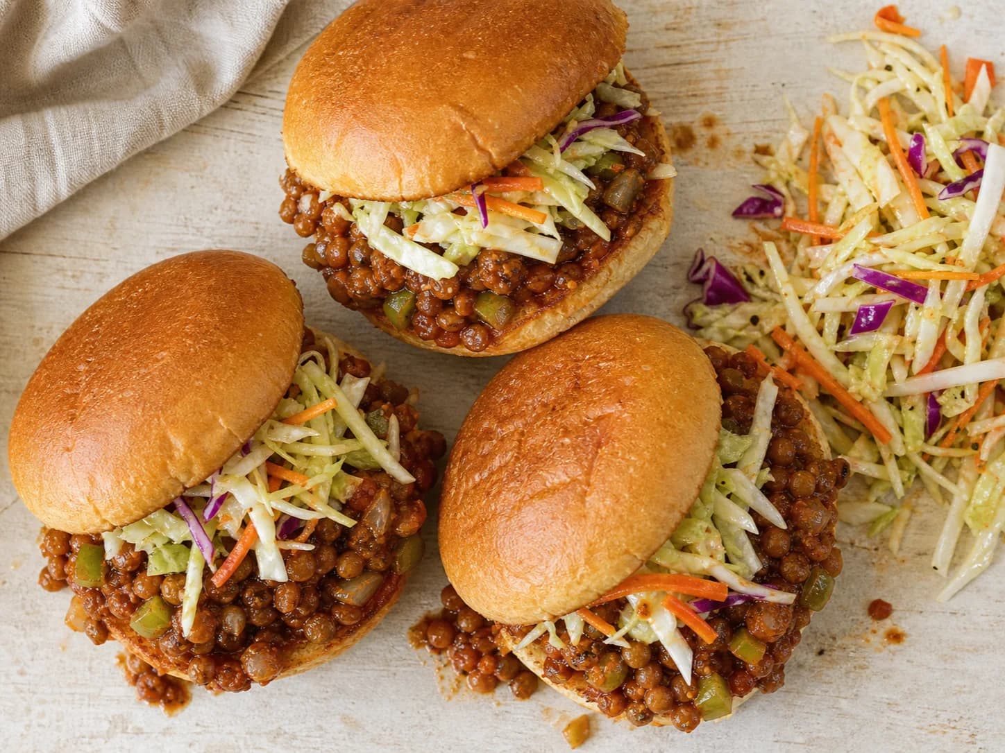 Overhead view of lentil sloppy-joe sandwiches & slaw, served as a family dinner.
