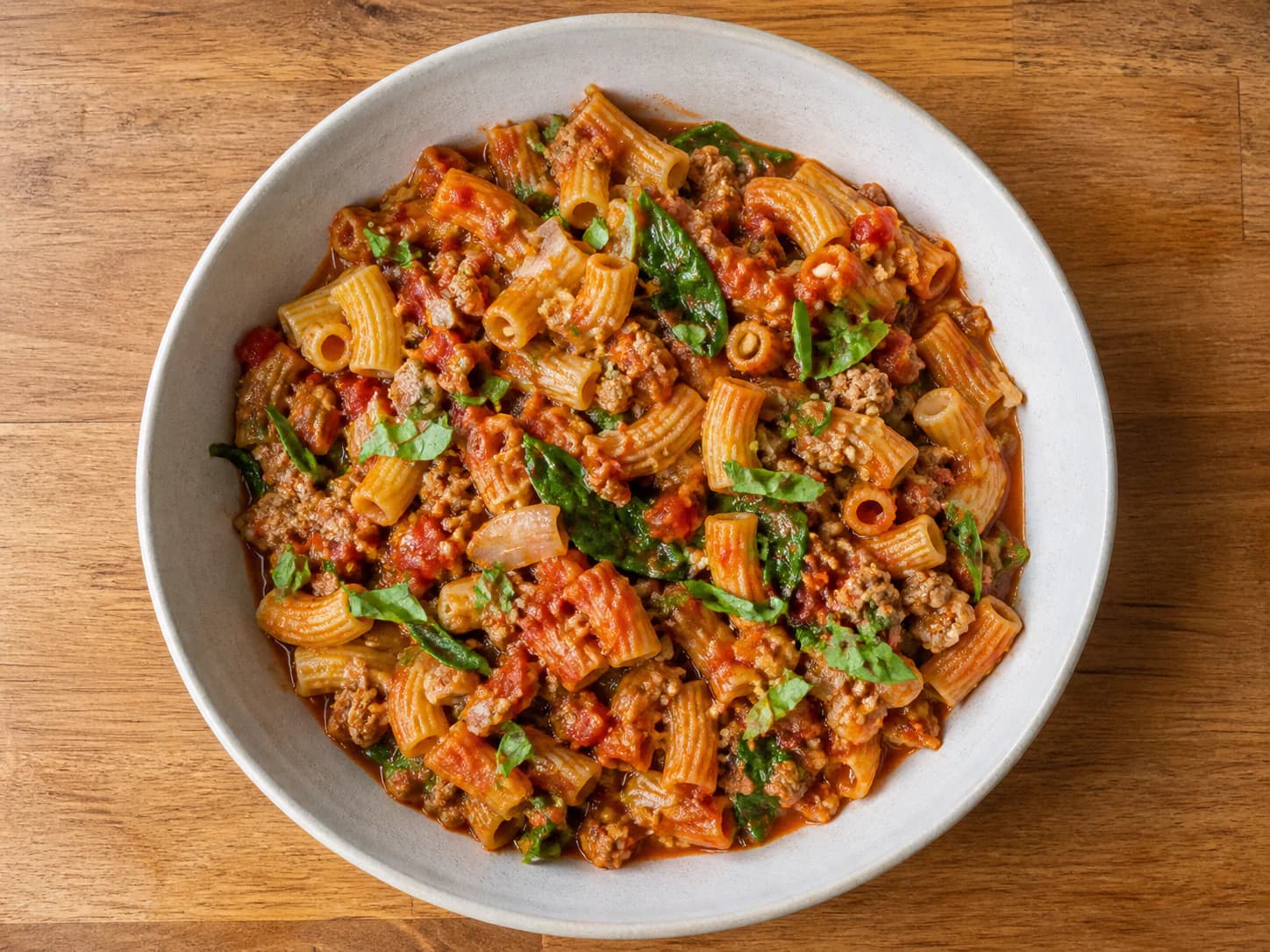 Rigatoni with ground turkey, rustic tomato sauce, spinach and basil in a shallow bowl.