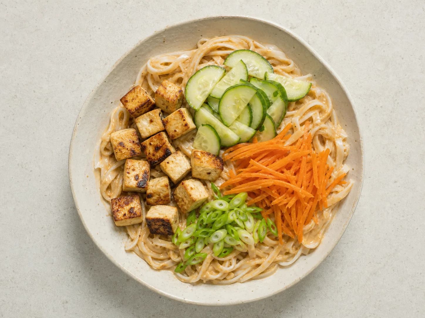 Overhead view of peanut-tofu rice noodles & cucumber, served as a family dinner.
