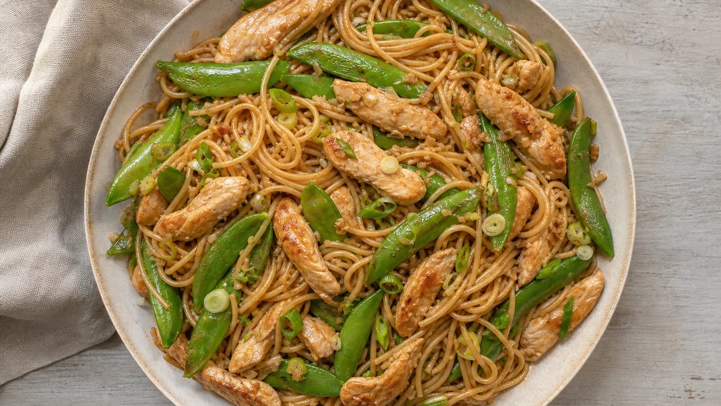 Overhead view of sesame chicken noodles & snap peas, served as a family dinner.