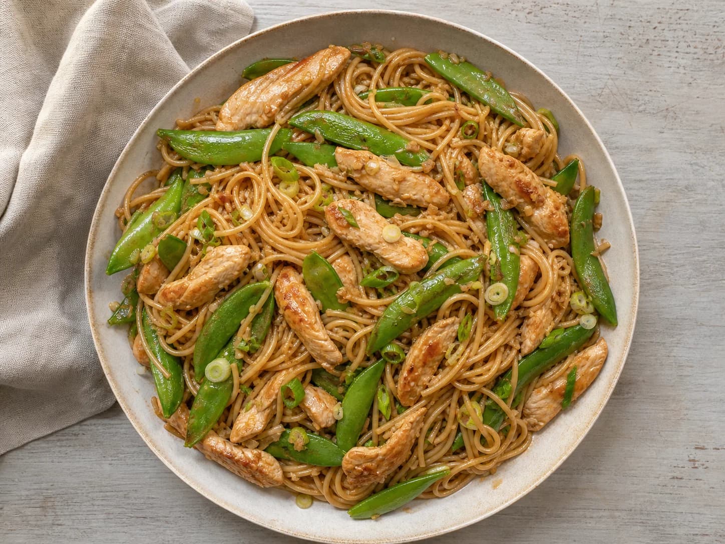 Overhead view of sesame chicken noodles & snap peas, served as a family dinner.