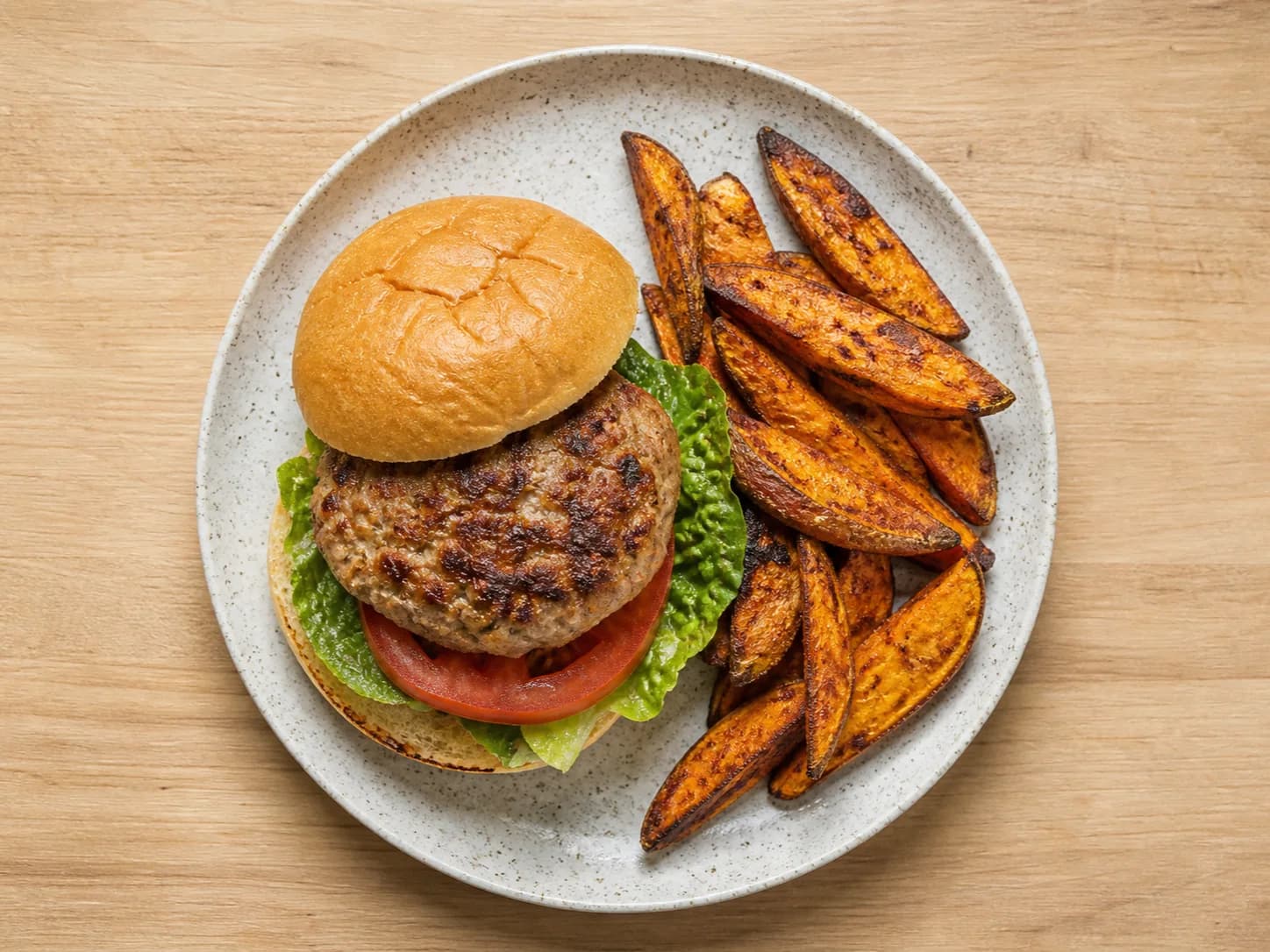 Overhead view of turkey burgers & sweet-potato wedges, served as a family dinner.
