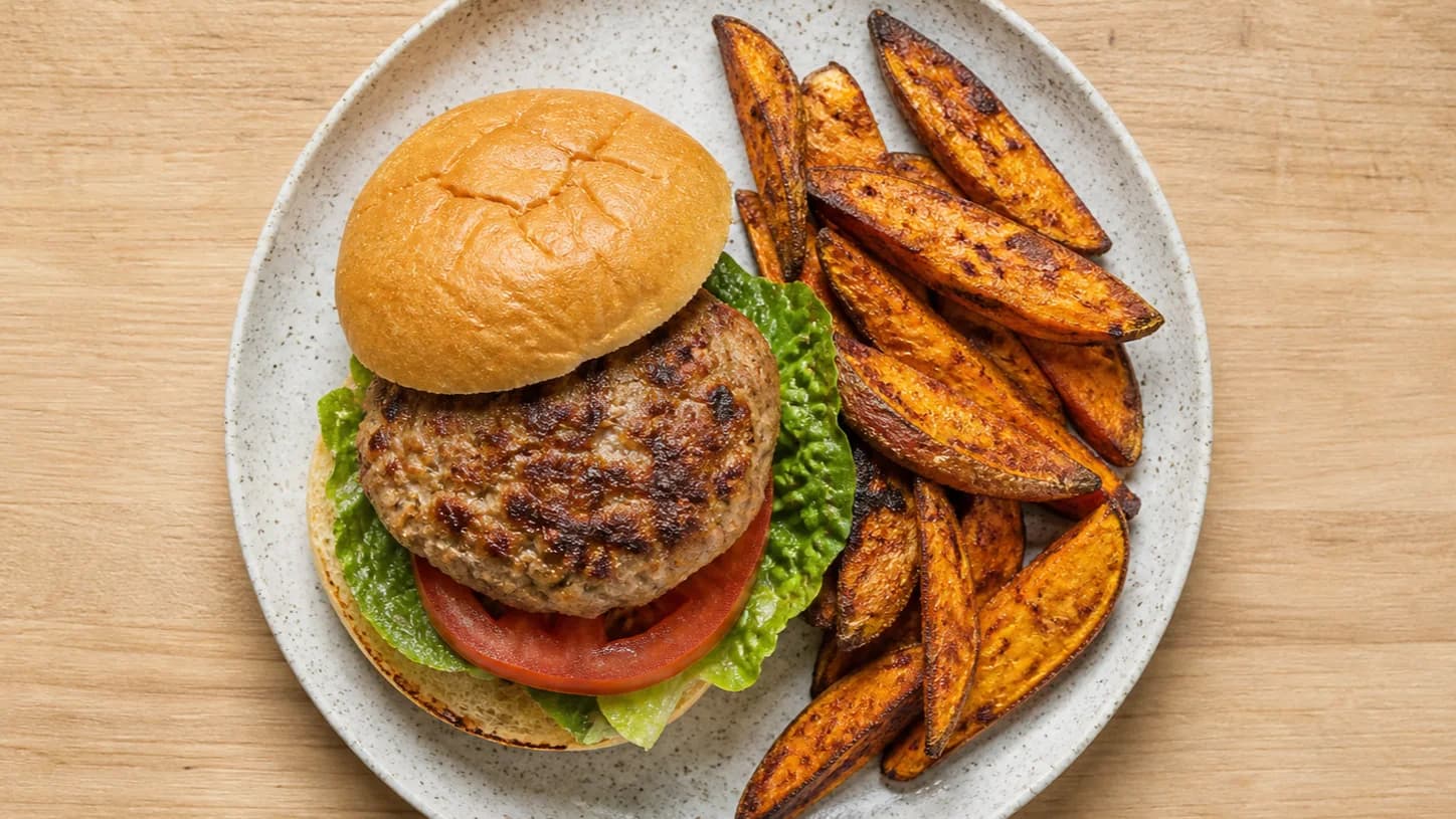 Overhead view of turkey burgers & sweet-potato wedges, served as a family dinner.