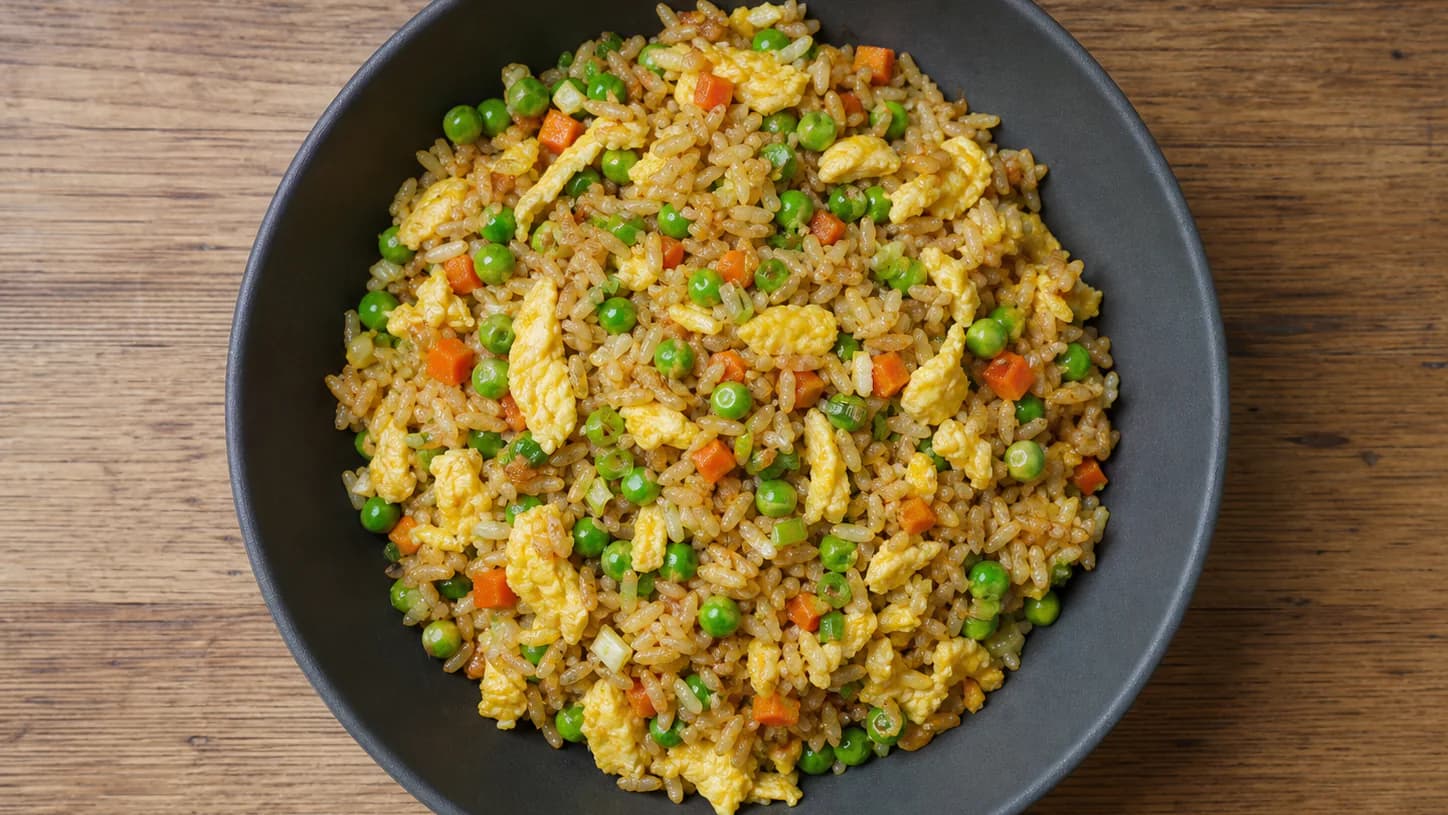 Vegetable fried rice with egg ribbons, peas, carrots and scallions in a dark bowl.